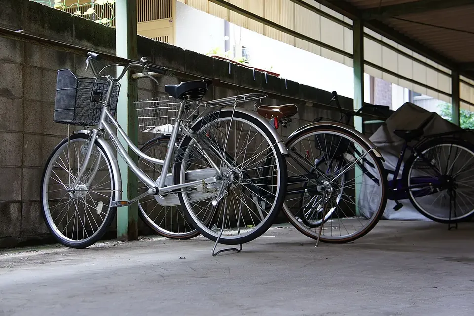 集合住宅の屋根付き駐輪場に並ぶ、前かごの付いた銀色のシティサイクルと数台の自転車