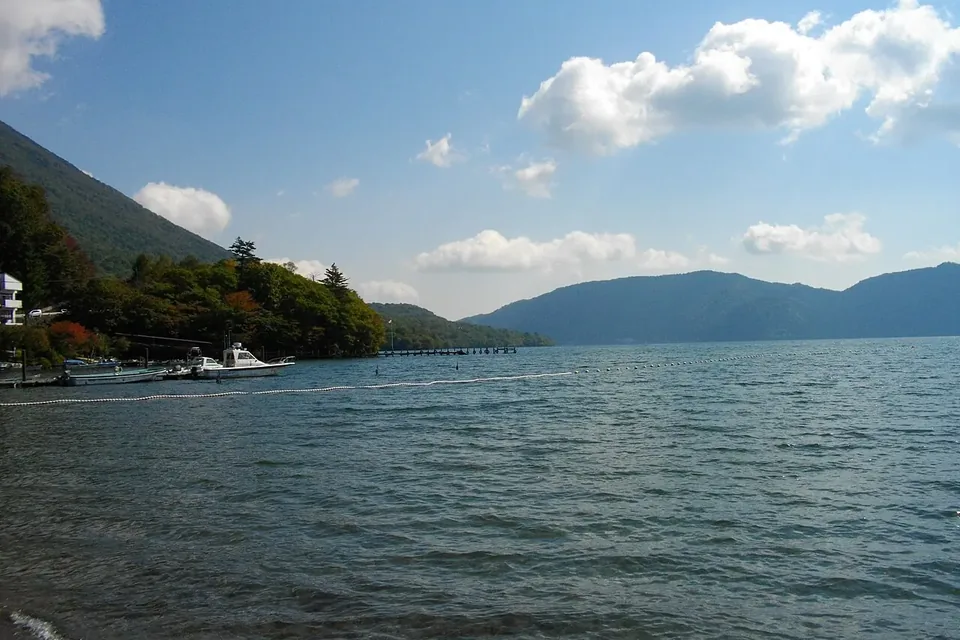 青空と白い雲の下、山々に囲まれて波立つ中禅寺湖の湖面